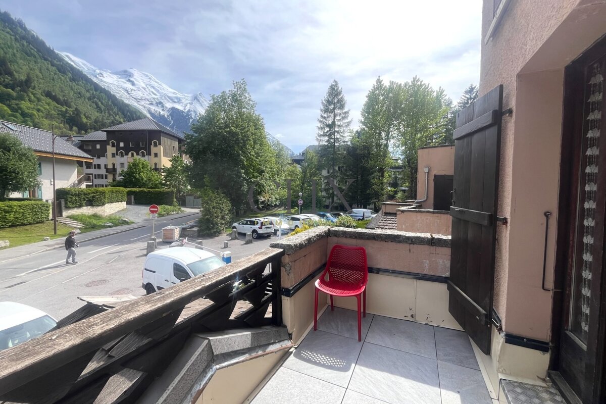 Balcony with a red chair overlooking a street and snow-covered mountains.