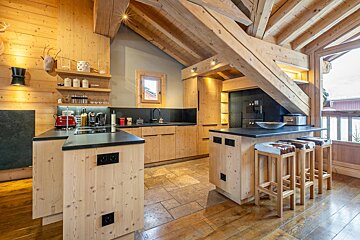 Cozy chalet kitchen with exposed wooden beams, light wood cabinets, black counters, and a breakfast bar with cowhide stools.