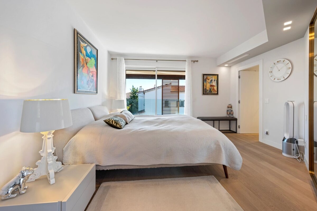 Bright, modern bedroom with a large white bed, a balcony window, hardwood floors, abstract art, and contemporary decor.