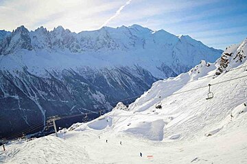 Skiers on a snowy slope with mountains in the background