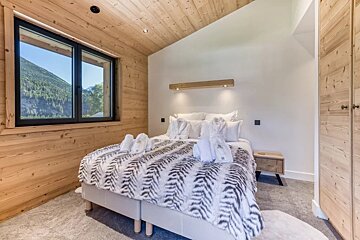 Cozy chalet bedroom with wood-paneled walls, a scenic mountain-view window, and a plush bed with a textured black-and-white throw.