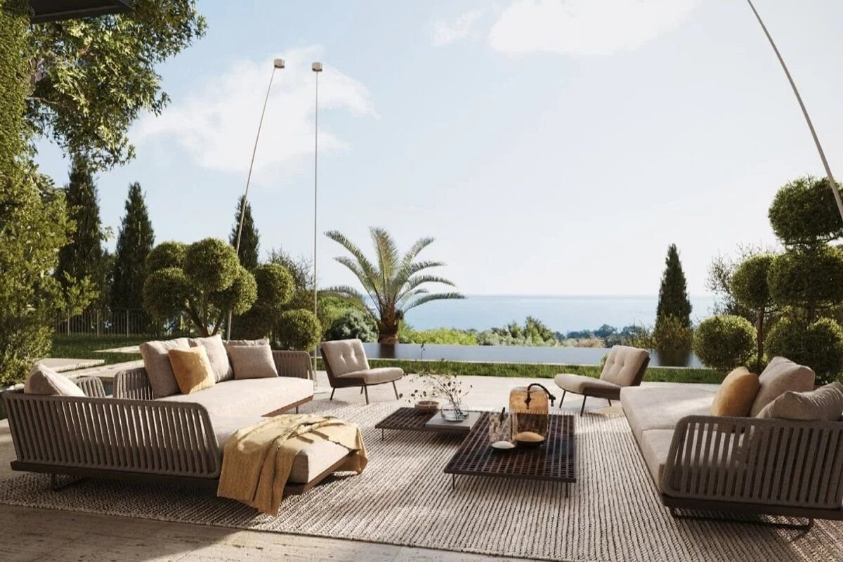 Stylish outdoor patio with modern furniture, lush greenery, and stunning ocean views under a clear sky.