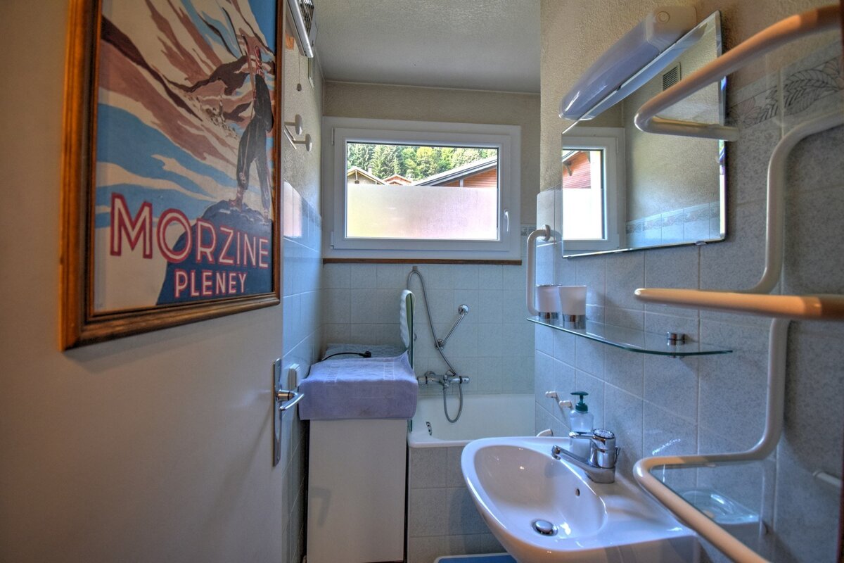 A cozy bathroom with a sink, bathtub, and window revealing trees. A