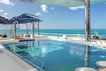 A large swimming pool surrounded by umbrellas overlooking the ocean