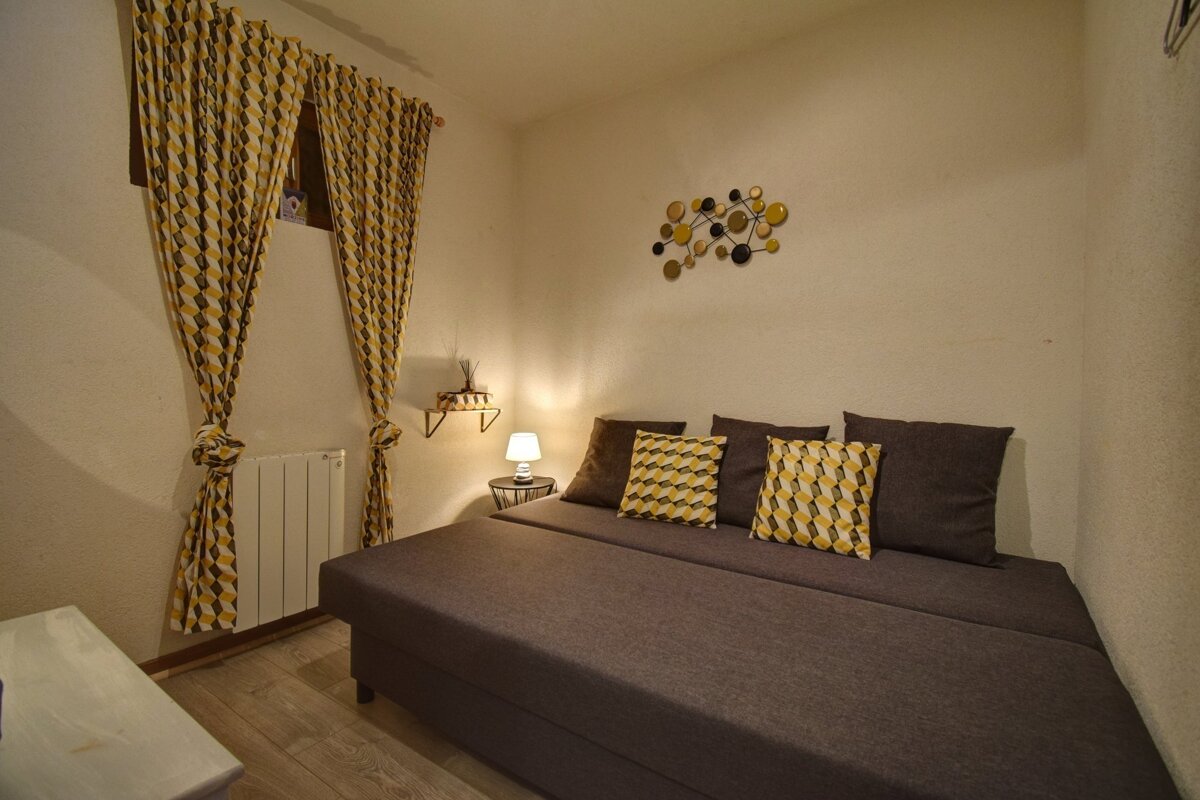 A cozy room with a brown sofa bed, yellow and brown patterned curtains and pillows, a small lamp, and geometric wall decor.