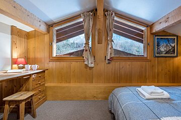 A bedroom with a bed a desk and two windows