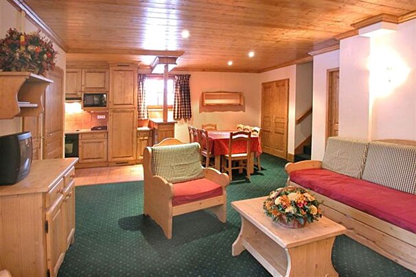 A cozy, open-plan chalet-style room with wooden furnishings, green carpet, and a kitchen, dining area, and living space. Warm, inviting atmosphere.