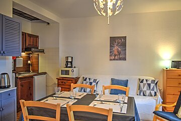 A cozy studio apartment with a kitchenette, dining table set for four, a sofa, and a deer painting on the wall.