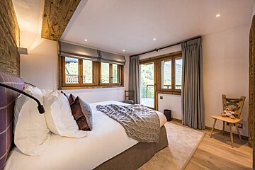 A bedroom with a large bed and a chair with a teddy bear on it