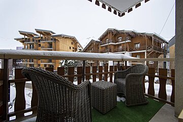 Two chairs and a table on a balcony with snow on the ground