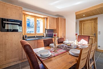 A bright, modern kitchen/dining room with warm wooden cabinetry, a set dining table, and a snowy view from the window, creating a cozy atmosphere.
