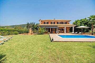 An orange villa with a swimming pool, spacious green lawn, and lush hills under a clear blue sky.