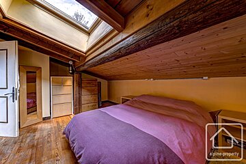 A cozy attic bedroom with wood-paneled ceilings, a large bed with a purple cover, and a skylight.