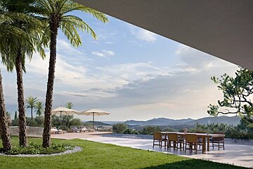 Modern luxury villa terrace with a dining table, palm trees, and lounge chairs overlooking a stunning mountain and coastal view.