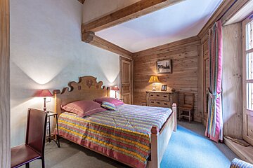 A cozy, rustic bedroom with wood paneling, exposed beams, a large bed with a colorful striped duvet, and warm bedside lamps.
