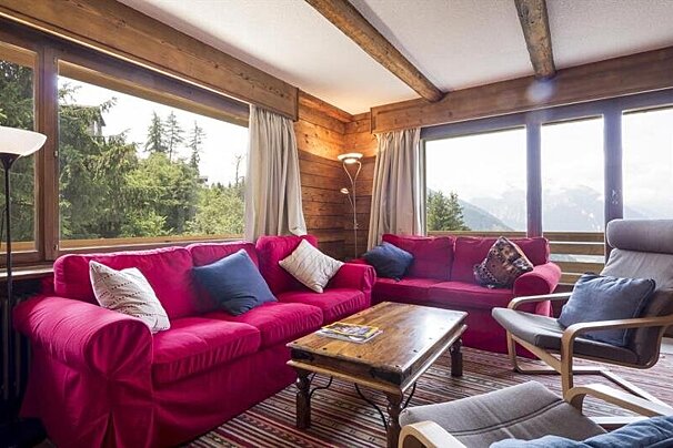Cozy chalet living room featuring bright red sofas, a wooden coffee table, and large windows showcasing beautiful mountain views.