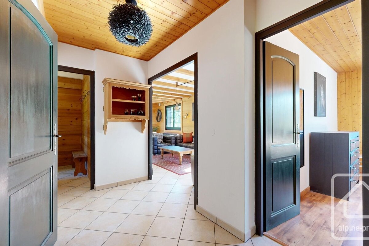 A bright hallway with warm wood ceilings and tiled floor. Features include open doorways to living spaces, a wall shelf, and a unique black light fixture.