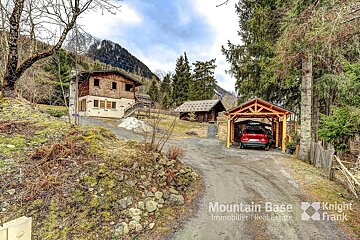 A red car is parked in front of a house that is for sale by mountain base