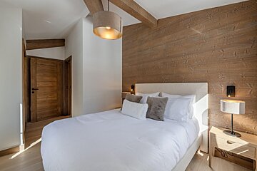 A bedroom with a wooden wall and a white bed