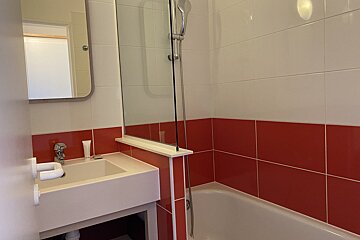 A clean bathroom with a white sink, mirror, and a bathtub/shower combo. The walls feature distinctive red and white tiling.