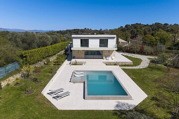 Aerial view of a modern two-story villa with a large swimming pool and lounge chairs on a spacious lawn.
