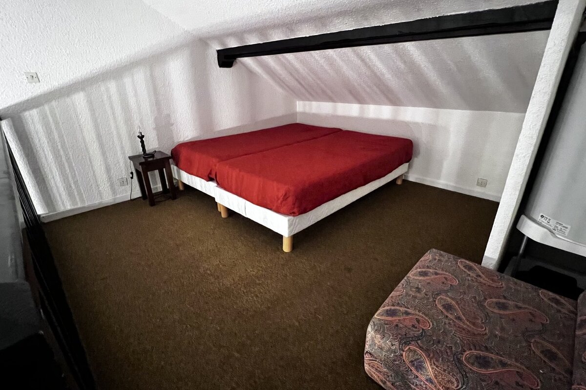 Cozy attic bedroom with a low sloped ceiling, brown carpet, and a double bed with bright red bedding.