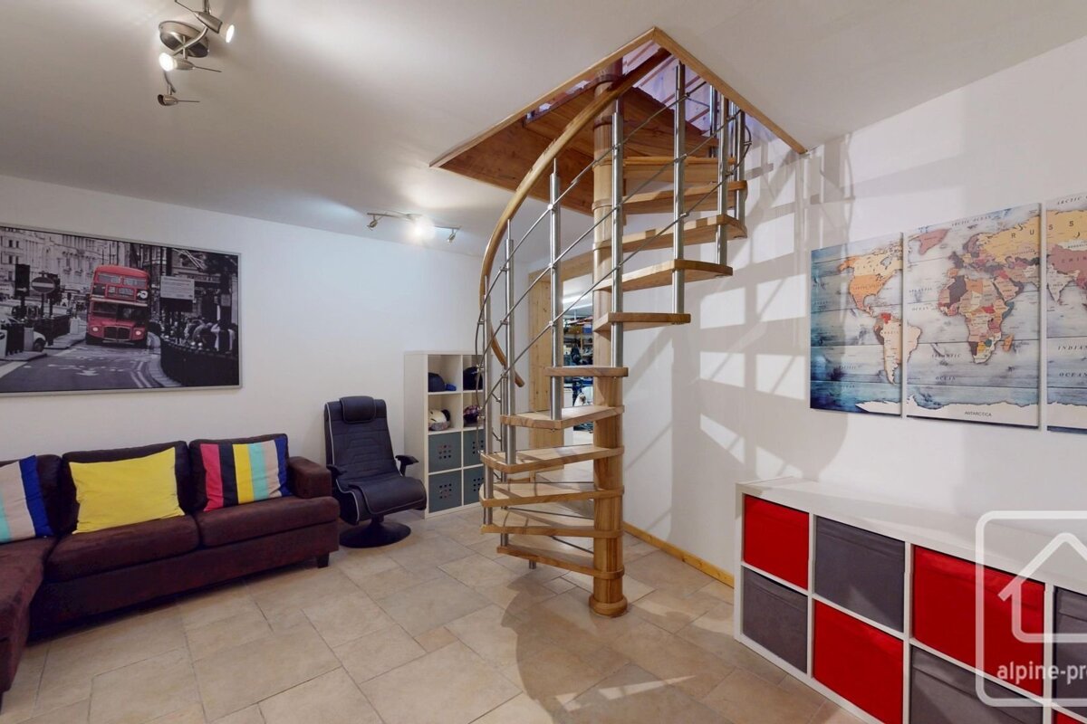 A modern room with a wooden and metal spiral staircase, a brown sofa with colorful cushions, a London bus print, and world map wall art.