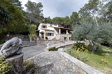 A stone walkway leads to a white house surrounded by trees
