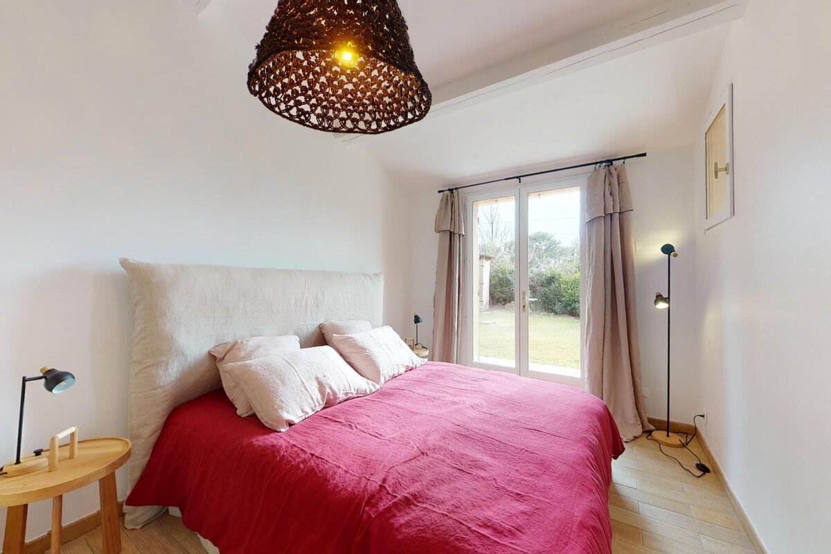 A bedroom with a red bed and a lamp hanging from the ceiling