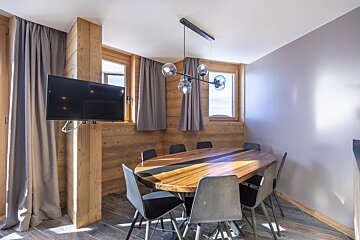 Modern rustic dining room with an oval wood table, gray chairs, stylish globe chandelier, and wood-paneled walls.