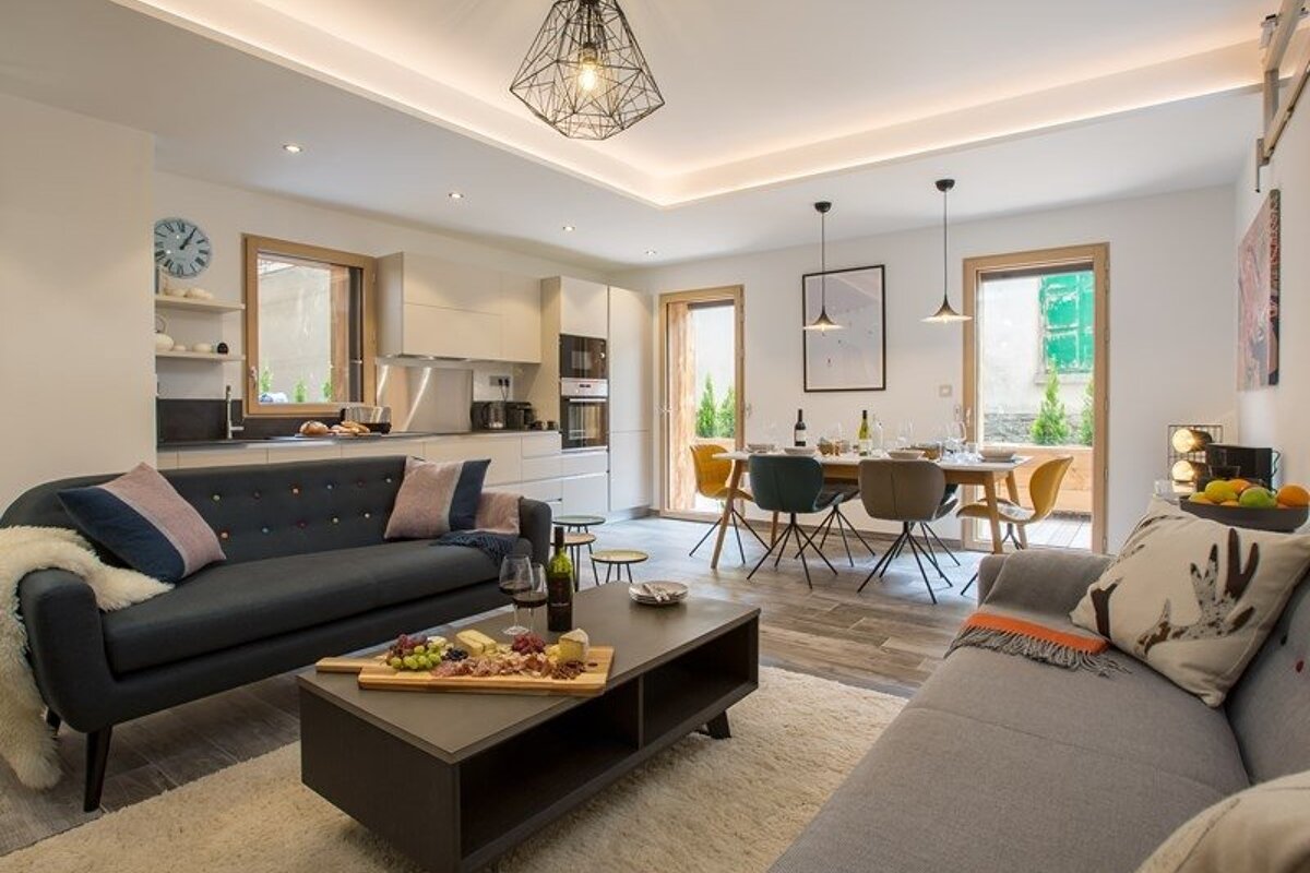 A chic, open-plan living room and dining area with a kitchen, featuring cozy sofas, a coffee table with wine, and stylish modern decor.