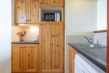 A compact kitchen with rustic pine wood cabinets, a built-in microwave, sink, hob, and a washing machine tucked under the counter.