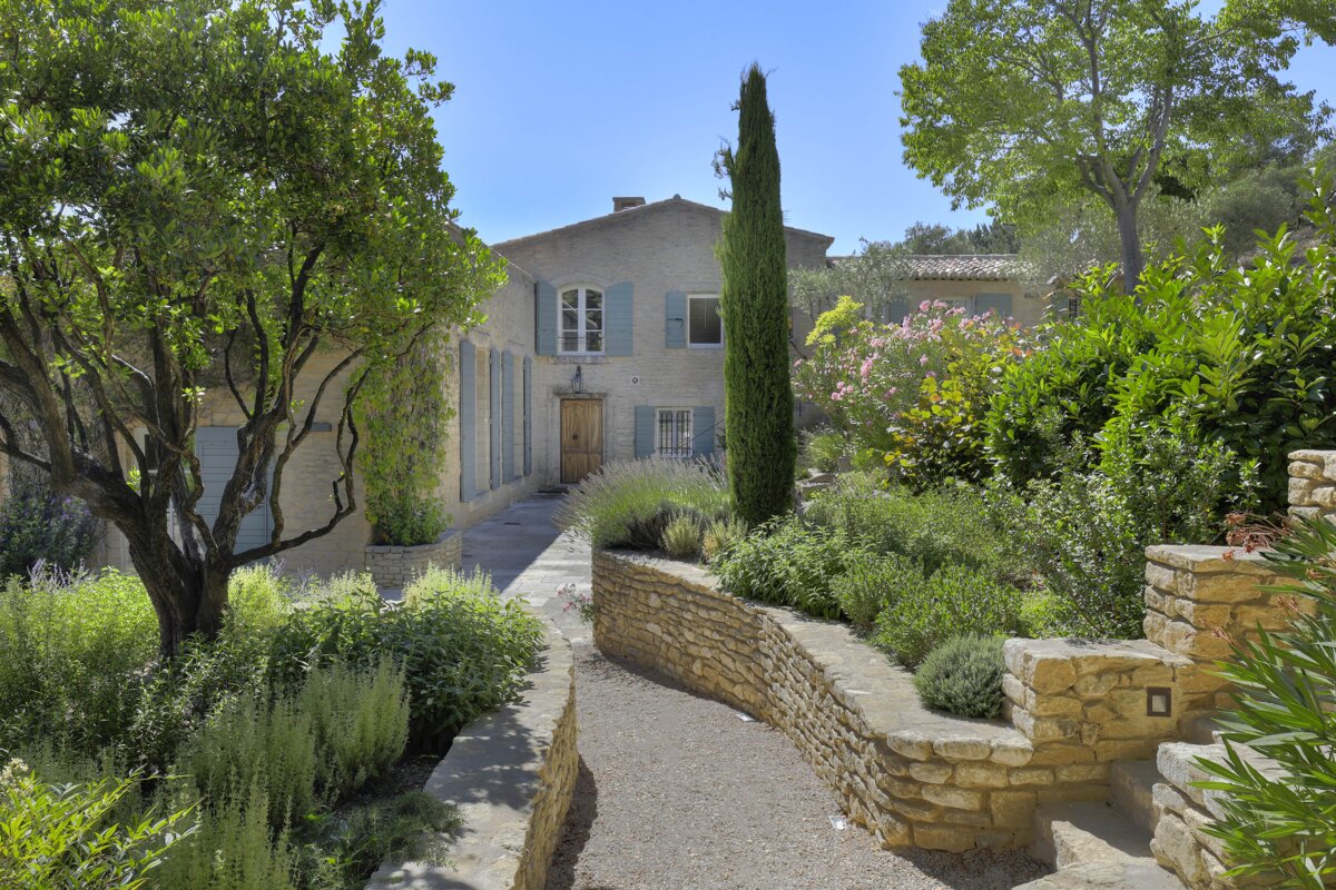 A stone walkway leads to a house with blue shutters