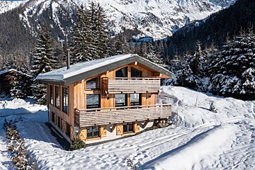 A wooden house in the snow with mountains in the background
