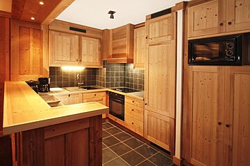 Cozy rustic kitchen featuring light pine wood cabinets, dark tile floor, black appliances, and a large wooden breakfast bar.