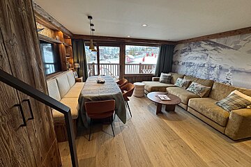 Modern rustic living/dining room in a ski lodge, featuring a large sectional sofa, wooden elements, and a view of snow-covered slopes.