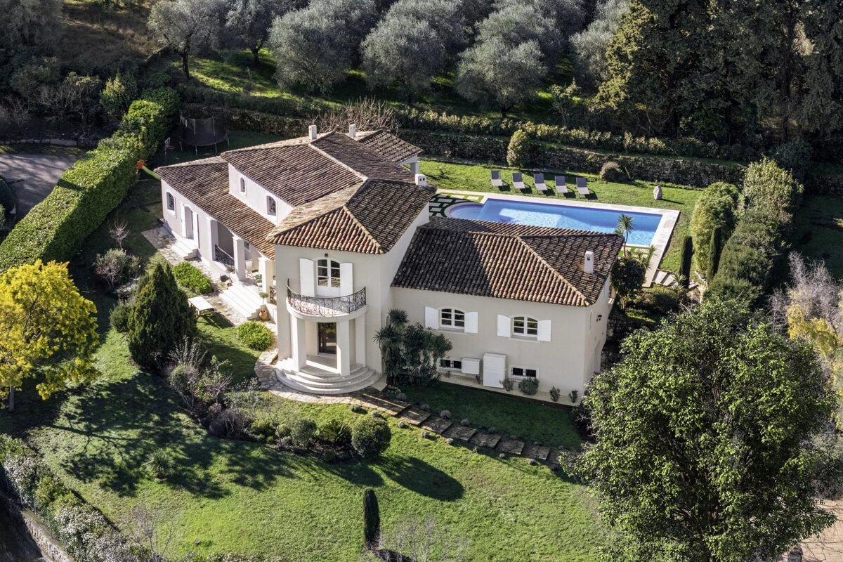 Aerial view of a luxury Mediterranean-style villa with a swimming pool, surrounded by a lush green lawn and trees.