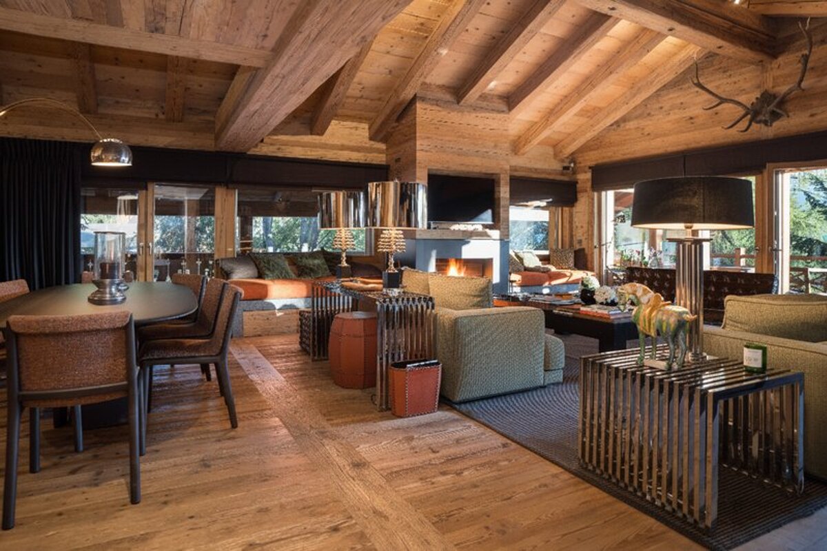 Luxurious, rustic chalet interior with exposed wood beams, a cozy living room, fireplace, and dining area.