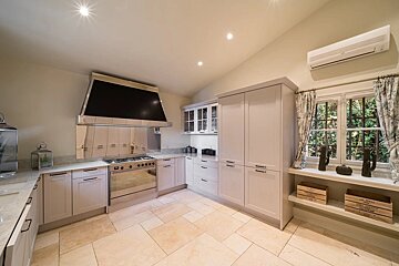 A modern kitchen with off-white cabinets, a large black range hood, beige tile flooring, and a window displaying small decorative items.