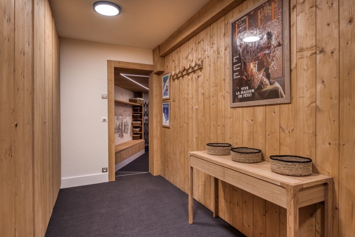 Cozy chalet entryway with warm wood paneling, ski posters, a console table with baskets, and a view into a modern boot room with built-in storage.