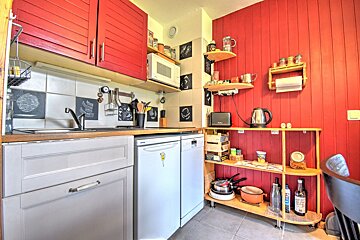 A compact kitchen with vibrant red cabinets and wall paneling, open wooden shelving, and small white appliances.