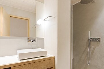 A modern minimalist bathroom featuring a white vessel sink on a wooden vanity, next to a sleek walk-in shower with grey walls.