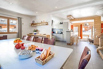 A dining room table with a basket of bread and jars of jam on it