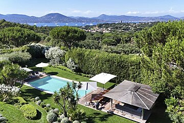 A luxury backyard with a swimming pool, cabana, and lush gardens overlooking a scenic bay and mountains.