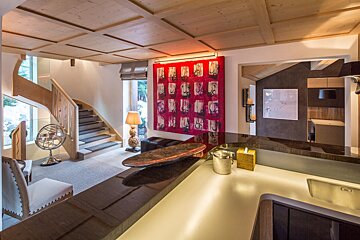 A luxurious modern interior featuring a wooden ceiling, curved staircase, large red abstract artwork, and a sleek bar/counter in the foreground.