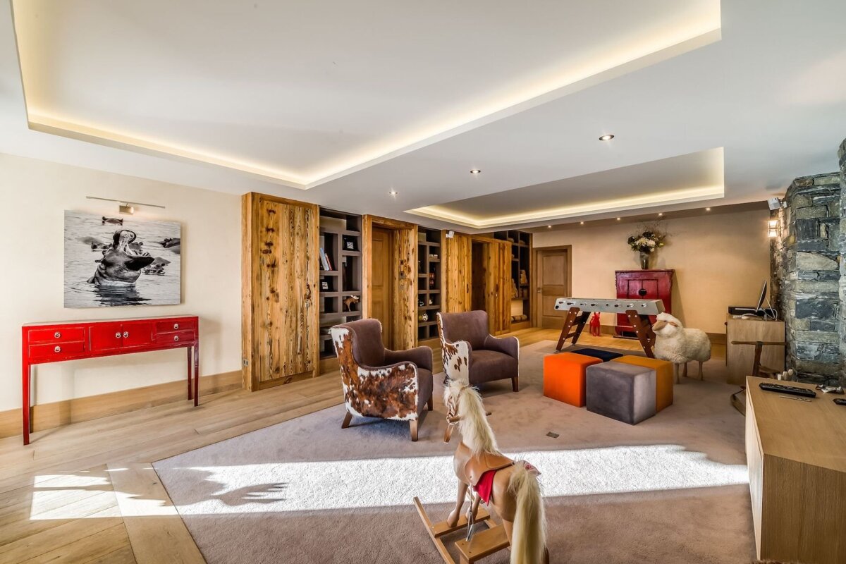 An eclectic living room with rustic wood cabinets, cowhide chairs, a foosball table, and unique decor like a rocking horse and hippo art.