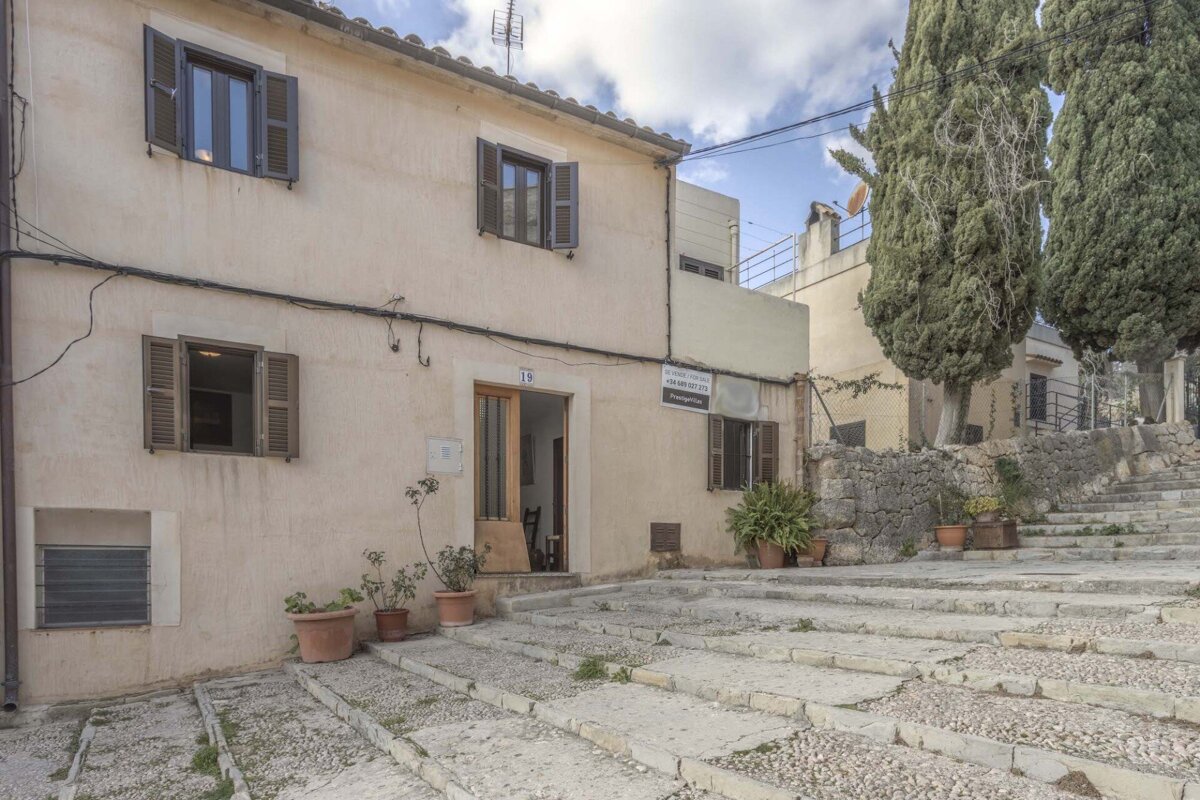 A light-colored house with brown shutters, potted plants, and a number