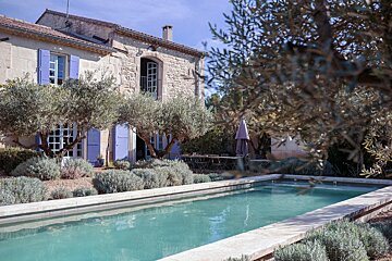 A large swimming pool in front of a house with purple shutters
