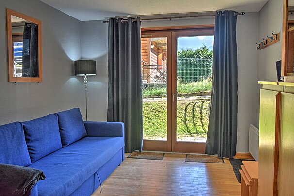 A cozy room features a bright blue sofa on a hardwood floor, facing glass patio doors leading to a green yard. Gray walls, a floor lamp, and a mirror are visible.