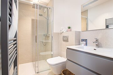 A modern bathroom featuring a glass-enclosed shower, a white toilet, and a grey vanity sink.